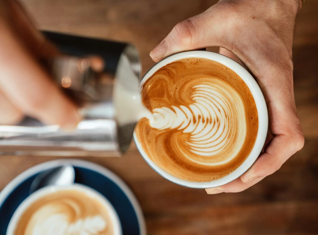 Close-up of barista pouring milk creating intricate latte art in coffee cup.