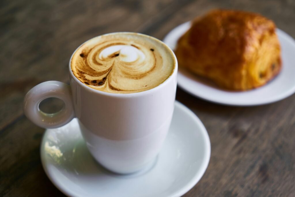 A delicious cappuccino with latte art next to a pastry on a wooden table, perfect for breakfast moments.